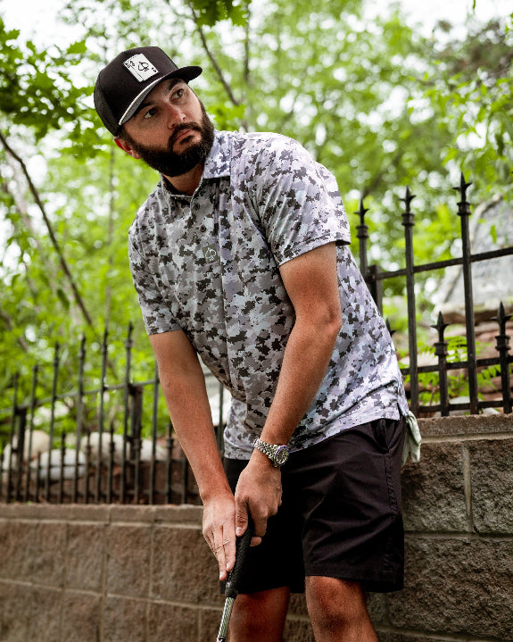Men’s Arctic Ops golf polo by Pins & Aces featuring an all-over gray, silver, and black camouflage print with short sleeves, collared neckline, and athletic performance fit.