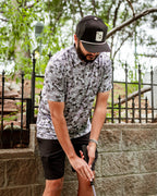 Men’s Arctic Ops golf polo by Pins & Aces featuring an all-over gray, silver, and black camouflage print with short sleeves, collared neckline, and athletic performance fit.