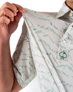 Men’s Altitude Adjustment golf polo by Pins & Aces featuring an off-white base with a subtle blue-green mountain range print, short sleeves, and athletic performance fit.