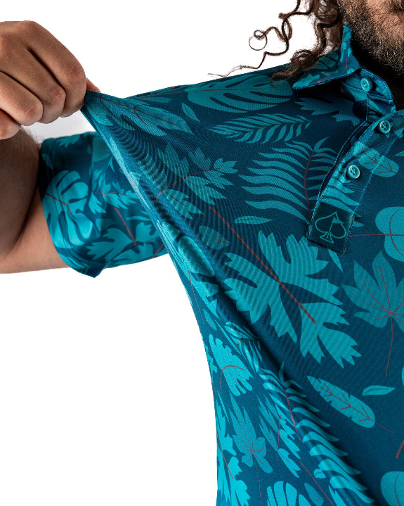 Men’s Cabana Nights golf polo by Pins & Aces featuring a blue and teal tropical leaf print, short sleeves, and athletic performance fit.