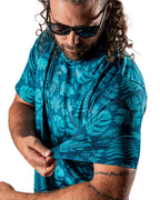 Men’s Cabana Nights golf polo by Pins & Aces featuring a blue and teal tropical leaf print, short sleeves, and athletic performance fit.