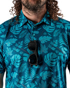 Men’s Cabana Nights golf polo by Pins & Aces featuring a blue and teal tropical leaf print, short sleeves, and athletic performance fit.