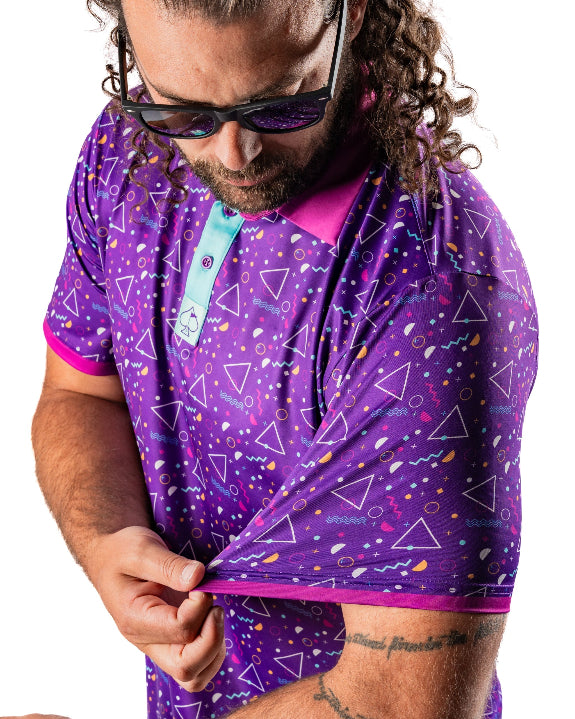 Men’s Eighties Arcade golf polo by Pins & Aces featuring a purple retro geometric print with pink and teal accents, short sleeves, and an athletic performance fit.
