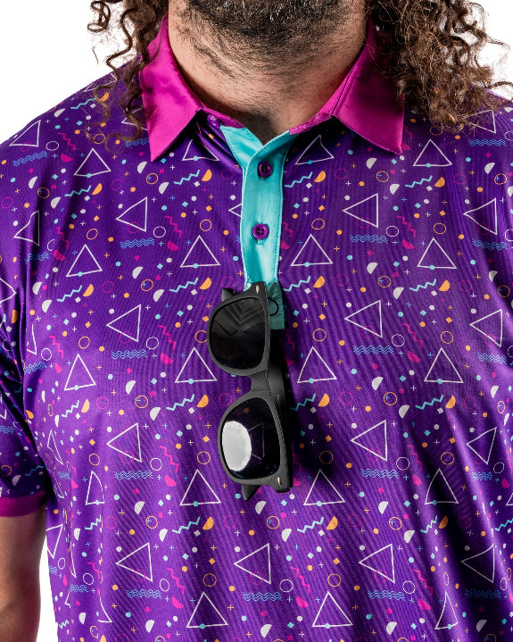 Men’s Eighties Arcade golf polo by Pins & Aces featuring a purple retro geometric print with pink and teal accents, short sleeves, and an athletic performance fit.