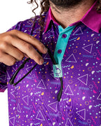 Men’s Eighties Arcade golf polo by Pins & Aces featuring a purple retro geometric print with pink and teal accents, short sleeves, and an athletic performance fit.