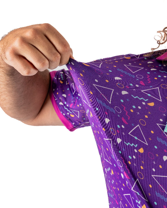 Men’s Eighties Arcade golf polo by Pins & Aces featuring a purple retro geometric print with pink and teal accents, short sleeves, and an athletic performance fit.