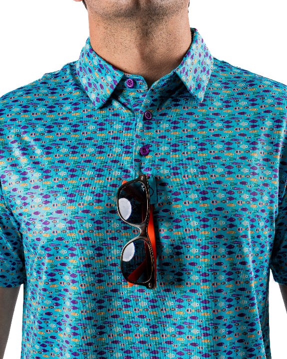 Men’s Fish & Drips golf polo by Pins & Aces featuring a bright aqua blue all-over fish print with colorful fishing-inspired details, short sleeves, and an athletic performance fit.