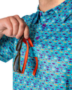 Men’s Fish & Drips golf polo by Pins & Aces featuring a bright aqua blue all-over fish print with colorful fishing-inspired details, short sleeves, and an athletic performance fit.