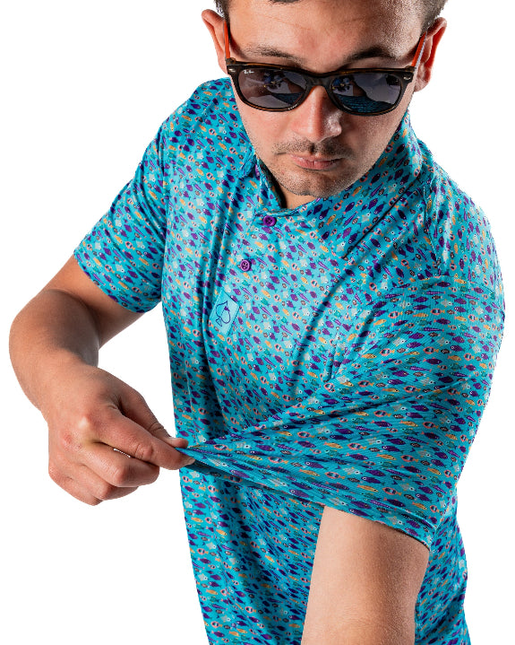 Men’s Fish & Drips golf polo by Pins & Aces featuring a bright aqua blue all-over fish print with colorful fishing-inspired details, short sleeves, and an athletic performance fit.