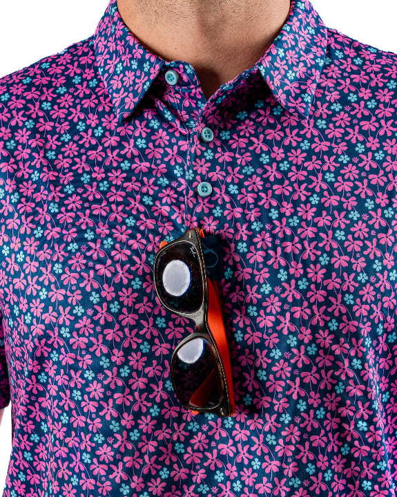 Men’s Full Bloom golf polo by Pins & Aces featuring an all-over bright pink floral pattern on a navy background with short sleeves and an athletic performance fit.