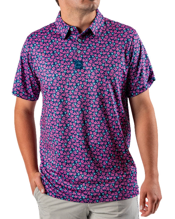Men’s Full Bloom golf polo by Pins & Aces featuring an all-over bright pink floral pattern on a navy background with short sleeves and an athletic performance fit.