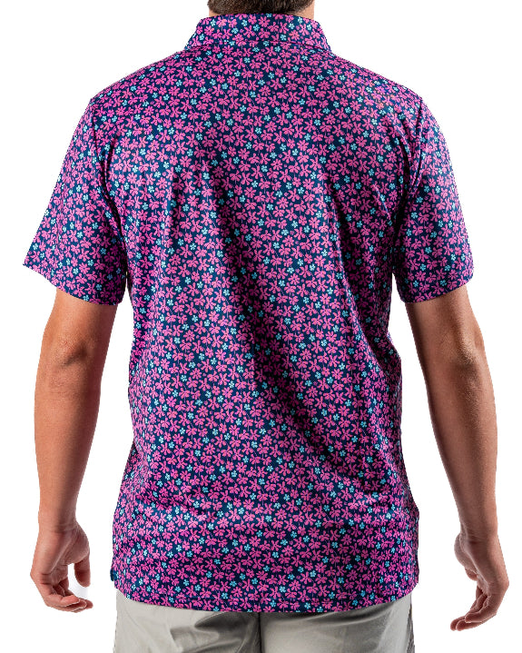 Men’s Full Bloom golf polo by Pins & Aces featuring an all-over bright pink floral pattern on a navy background with short sleeves and an athletic performance fit.