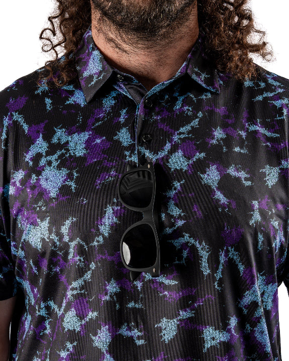 Men’s Moon Burn golf polo by Pins & Aces featuring an abstract purple, blue, and black cosmic-inspired pattern with short sleeves and an athletic performance fit.