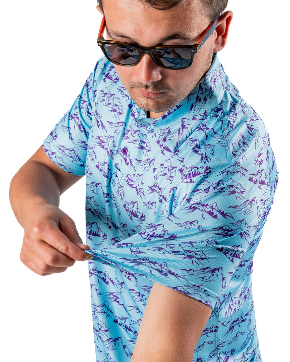 Men’s Purple Majesty golf polo by Pins & Aces featuring an aqua blue base with an all-over purple illustrated mountain print, short sleeves, and athletic performance fit.