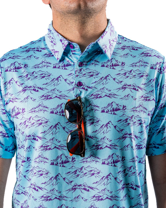 Men’s Purple Majesty golf polo by Pins & Aces featuring an aqua blue base with an all-over purple illustrated mountain print, short sleeves, and athletic performance fit.