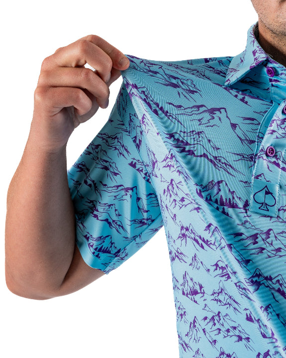 Men’s Purple Majesty golf polo by Pins & Aces featuring an aqua blue base with an all-over purple illustrated mountain print, short sleeves, and athletic performance fit.