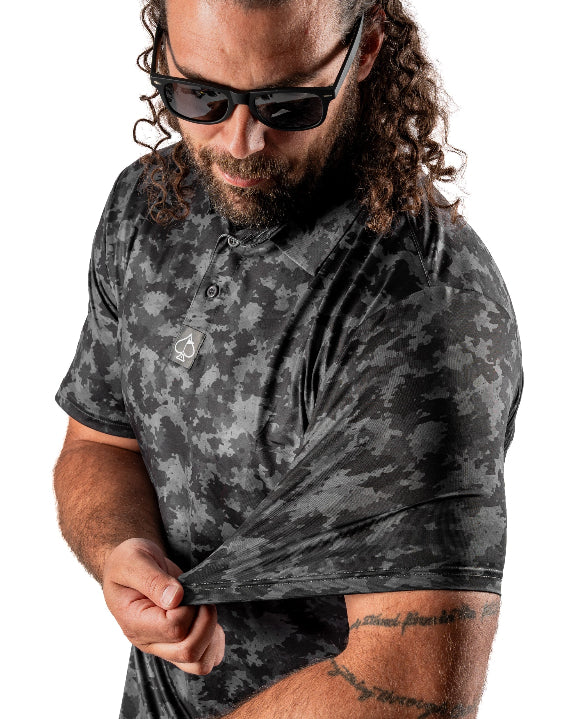 Men’s Shadow Ops black camo golf polo by Pins & Aces featuring a tonal black and charcoal camouflage pattern, short sleeves, collared neckline, and athletic fit.