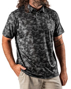 Men’s Shadow Ops black camo golf polo by Pins & Aces featuring a tonal black and charcoal camouflage pattern, short sleeves, collared neckline, and athletic fit.