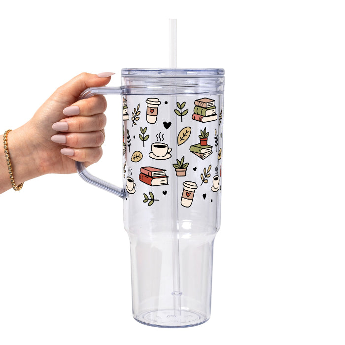 Clear glass mug with bamboo lid and straw featuring a wraparound book lover design with stacked books, coffee cups, potted plants, leafy branches and small black hearts.