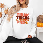 Thick Thighs and Pumpkin Pies fall sweatshirt featuring a funny Thanksgiving-inspired graphic on a cozy unisex crewneck in White