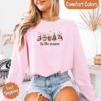 ’Tis The Season Comfort Colors long sleeve Christmas shirt featuring a festive holiday graphic on a soft garment-dyed 100% cotton tee in Light Pink