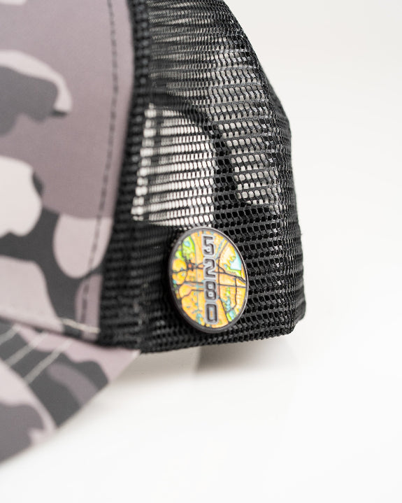 Urban Camo trucker golf hat by Pins & Aces featuring a gray, black, and white camouflage print, embroidered black spade logo, black mesh back, curved bill, and snapback design.
