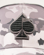 Urban Camo trucker golf hat by Pins & Aces featuring a gray, black, and white camouflage print, embroidered black spade logo, black mesh back, curved bill, and snapback design.