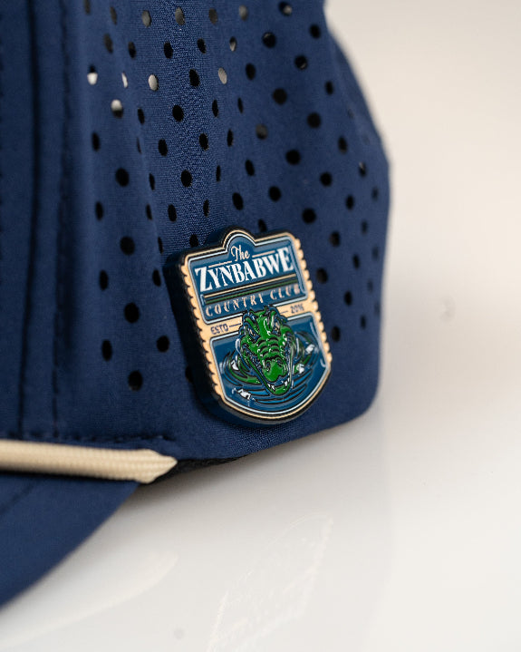 Zynbabwe Country Club Navy perforated rope golf hat by Pins & Aces with adjustable snapback, magnetic ball marker holder, and matching golf ball marker.
