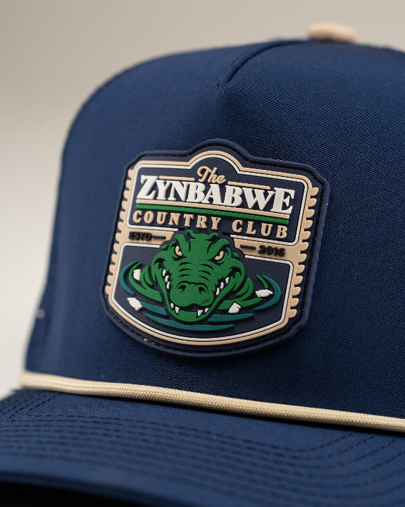 Zynbabwe Country Club Navy perforated rope golf hat by Pins & Aces with adjustable snapback, magnetic ball marker holder, and matching golf ball marker.